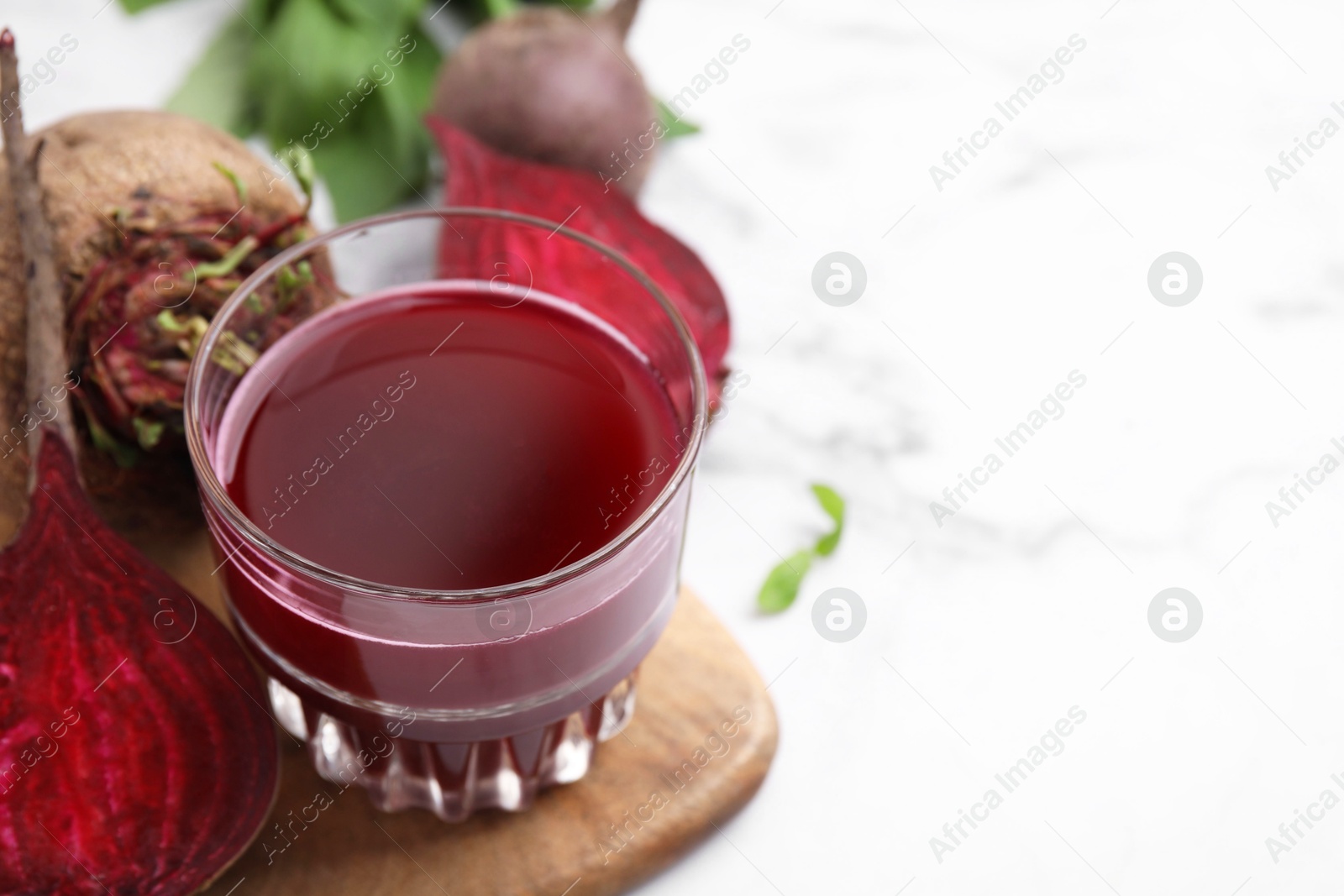 Photo of Fresh beet juice in glass and ripe vegetables on white marble table, closeup. Space for text