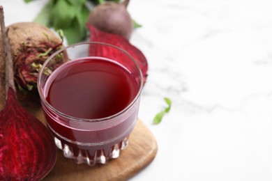 Photo of Fresh beet juice in glass and ripe vegetables on white marble table, closeup. Space for text