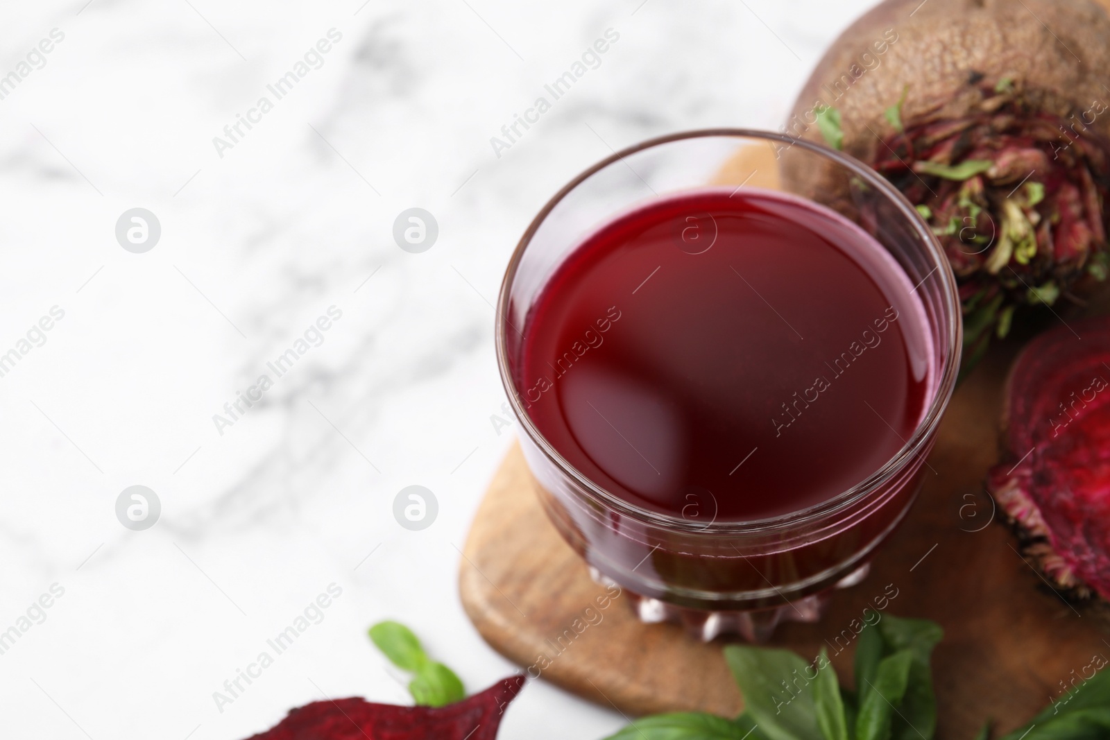 Photo of Fresh beet juice in glass, ripe vegetables and basil on white table, closeup. Space for text