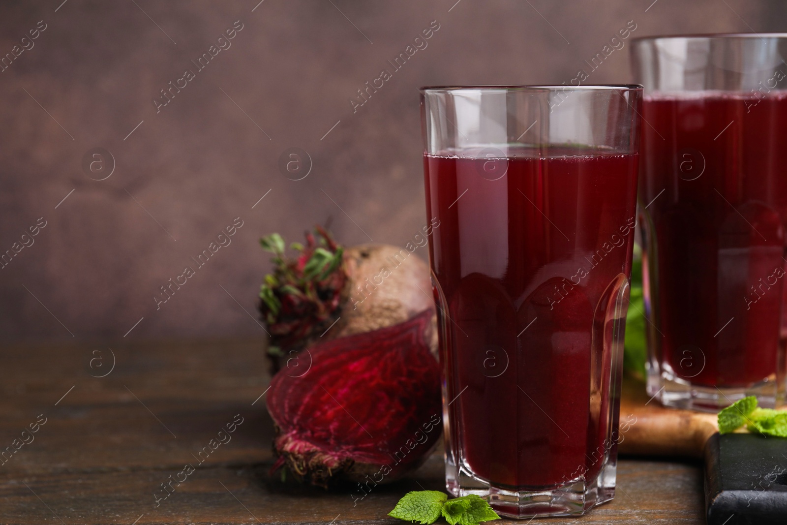 Photo of Fresh beet juice in glasses and ripe vegetables on wooden table, closeup. Space for text