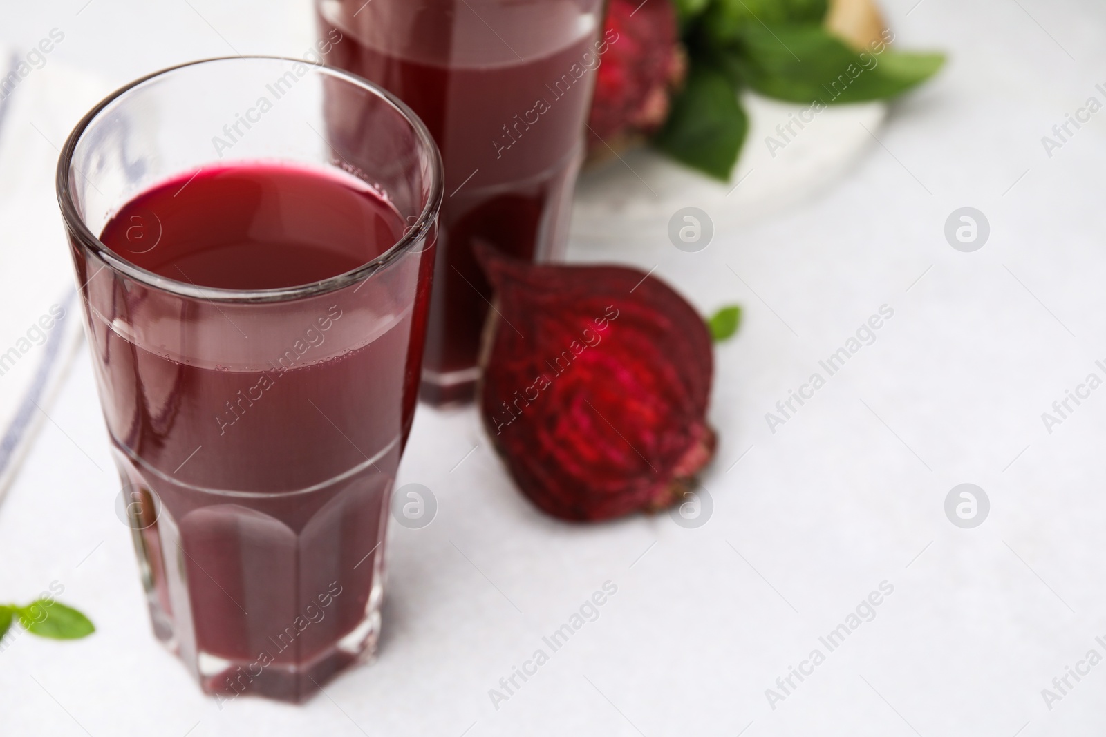 Photo of Fresh beet juice in glasses on light table, closeup. Space for text