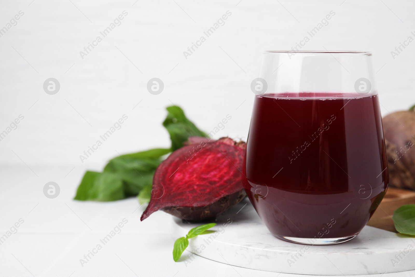 Photo of Fresh beet juice in glass and ripe vegetables on white tiled table, closeup. Space for text