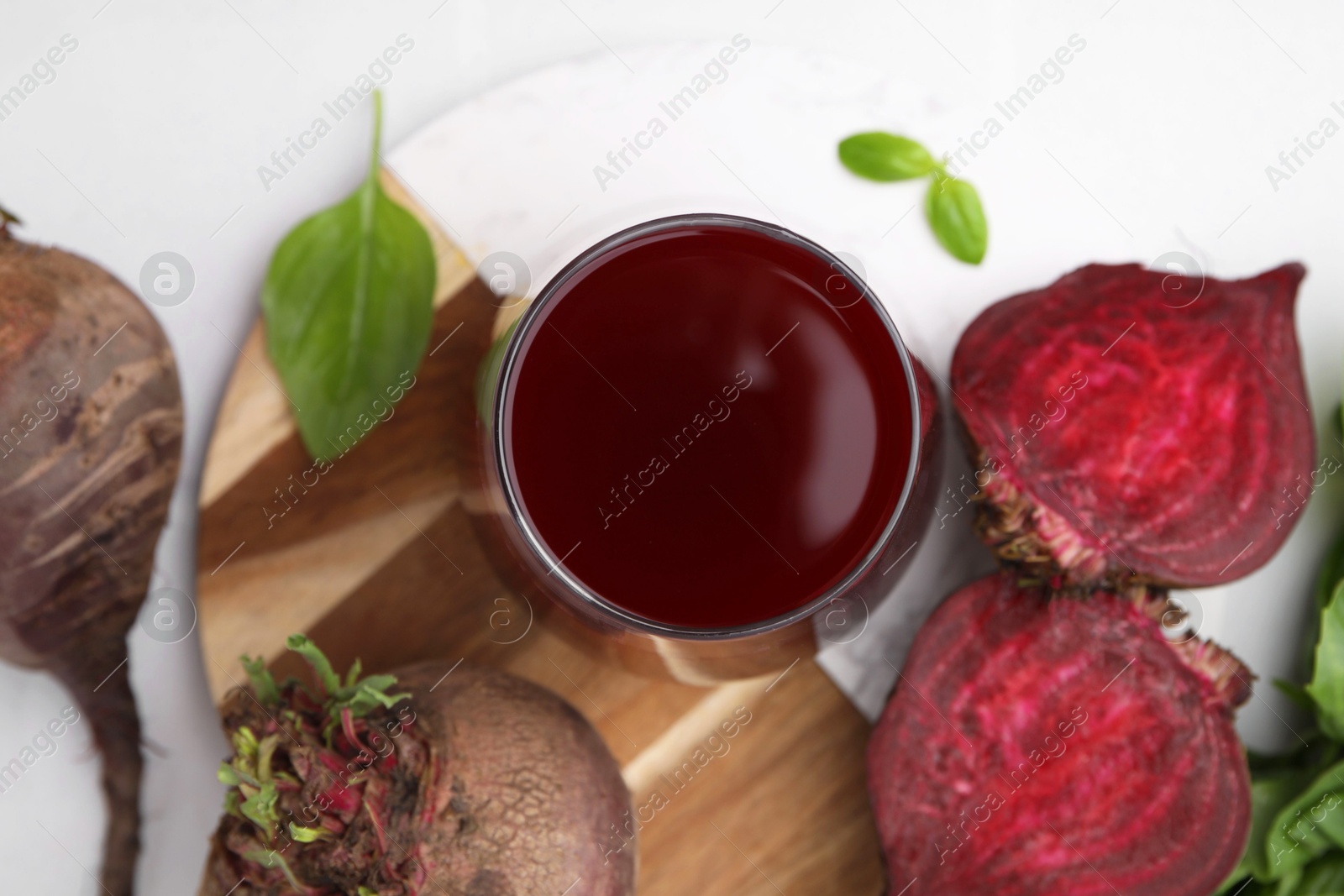 Photo of Fresh beet juice in glass and ripe vegetables on white table, flat lay