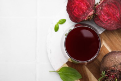 Photo of Fresh beet juice in glass, ripe vegetables and basil on white table, flat lay. Space for text