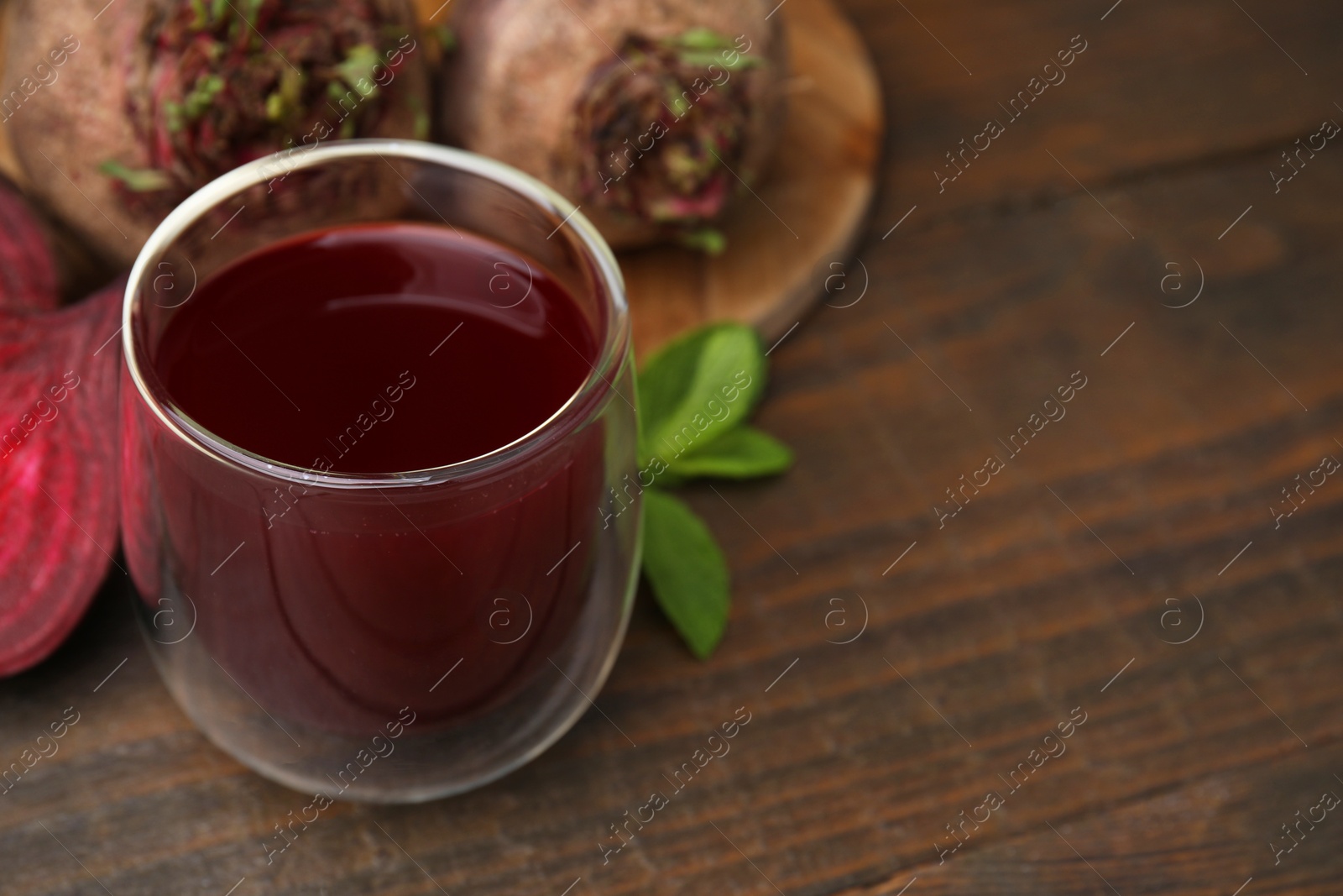 Photo of Fresh beet juice in glass, ripe vegetables and mint on wooden table, closeup. Space for text