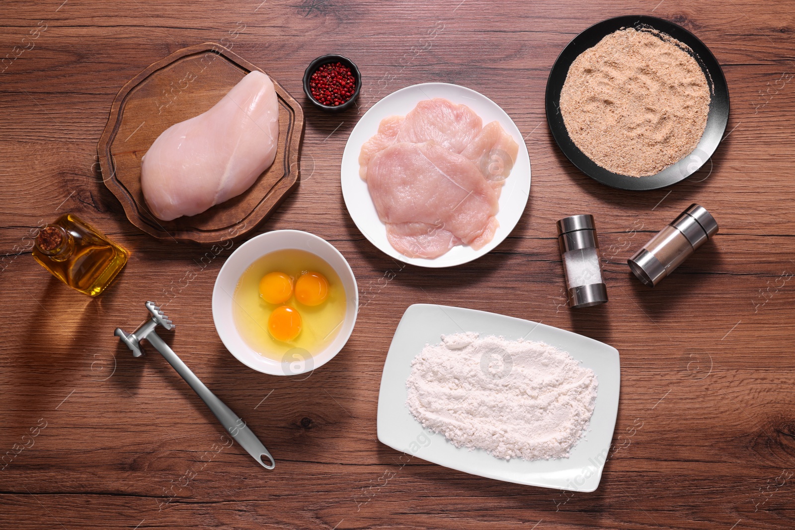 Photo of Making schnitzel. Raw meat, spices, yolks, bread crumbs and tenderizer on wooden table, flat lay