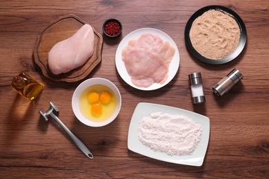 Making schnitzel. Raw meat, spices, yolks, bread crumbs and tenderizer on wooden table, flat lay