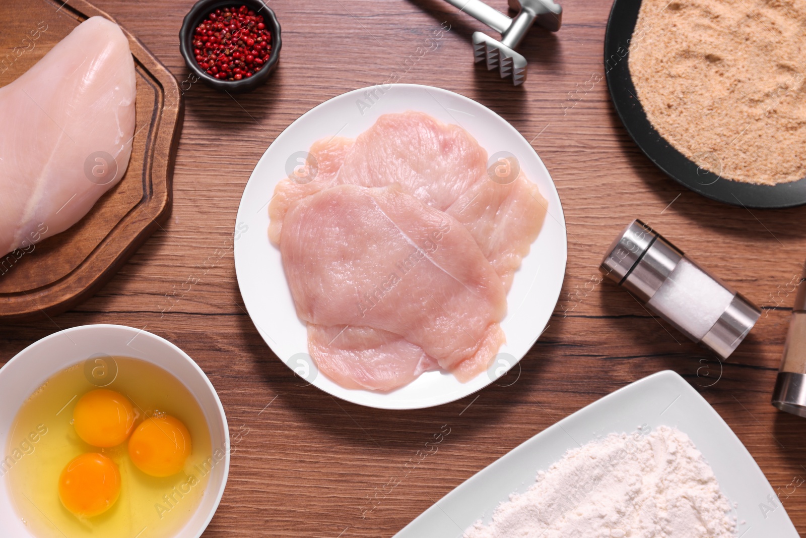 Photo of Making schnitzel. Raw meat, spices, yolks, bread crumbs and tenderizer on wooden table, flat lay