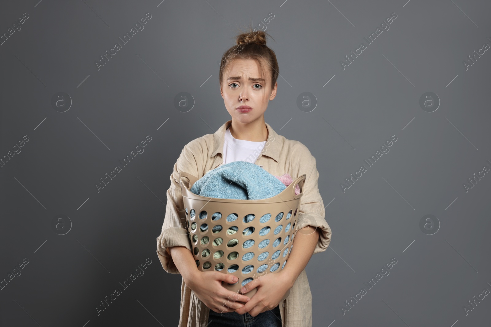 Photo of Tired housewife with basket full of laundry on grey background