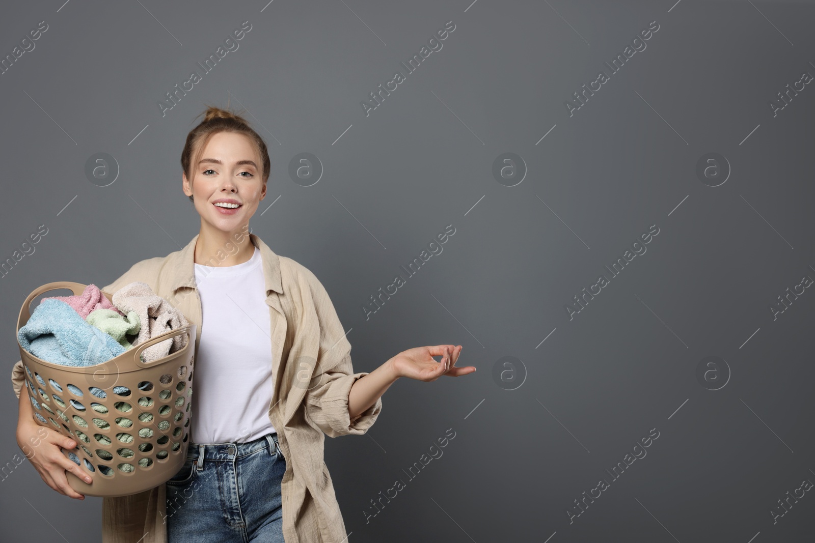 Photo of Happy young housewife with basket full of laundry on grey background. Space for text