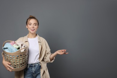 Happy young housewife with basket full of laundry on grey background. Space for text