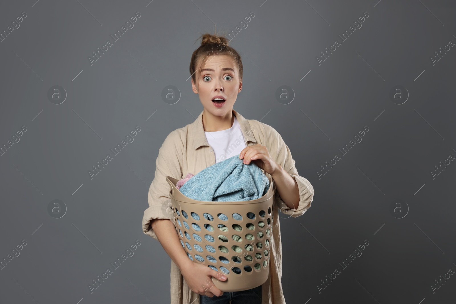 Photo of Tired housewife with basket full of laundry on grey background