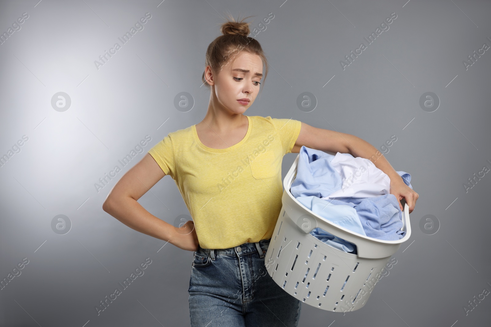 Photo of Tired housewife with basket full of laundry on grey background