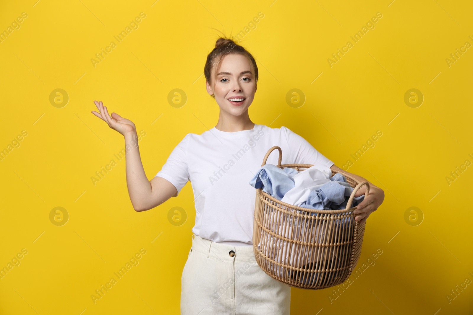 Photo of Happy young housewife with basket full of laundry on yellow background