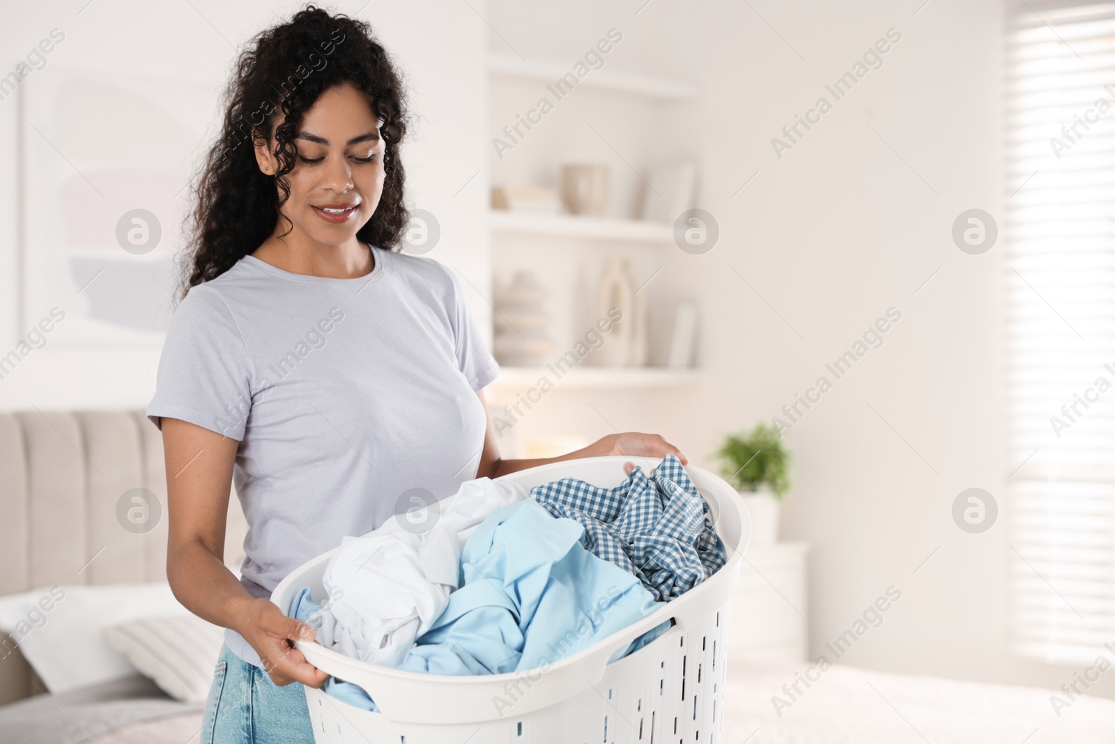 Photo of Happy woman with basket full of laundry in bedroom, space for text