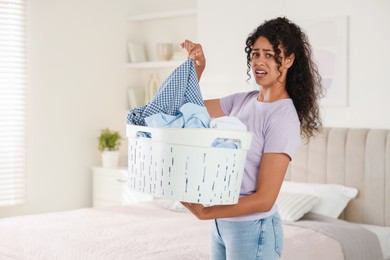 Displeased woman with basket full of laundry in bedroom, space for text