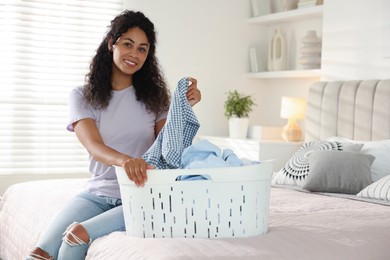 Happy woman with basket full of laundry on bed at home