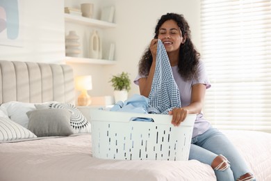 Happy woman with basket full of laundry on bed at home