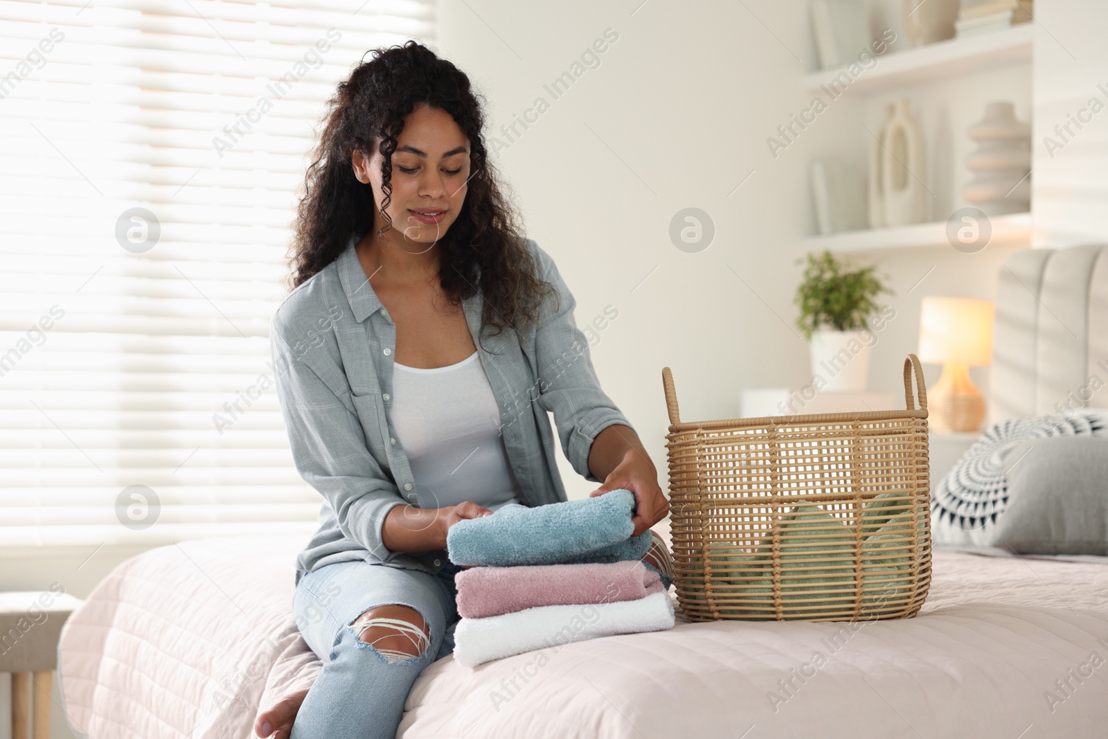 Photo of Woman with laundry near basket on bed at home