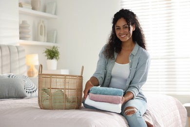 Happy woman with laundry near basket on bed at home