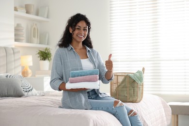 Photo of Happy woman with laundry near basket showing thumbs up on bed at home