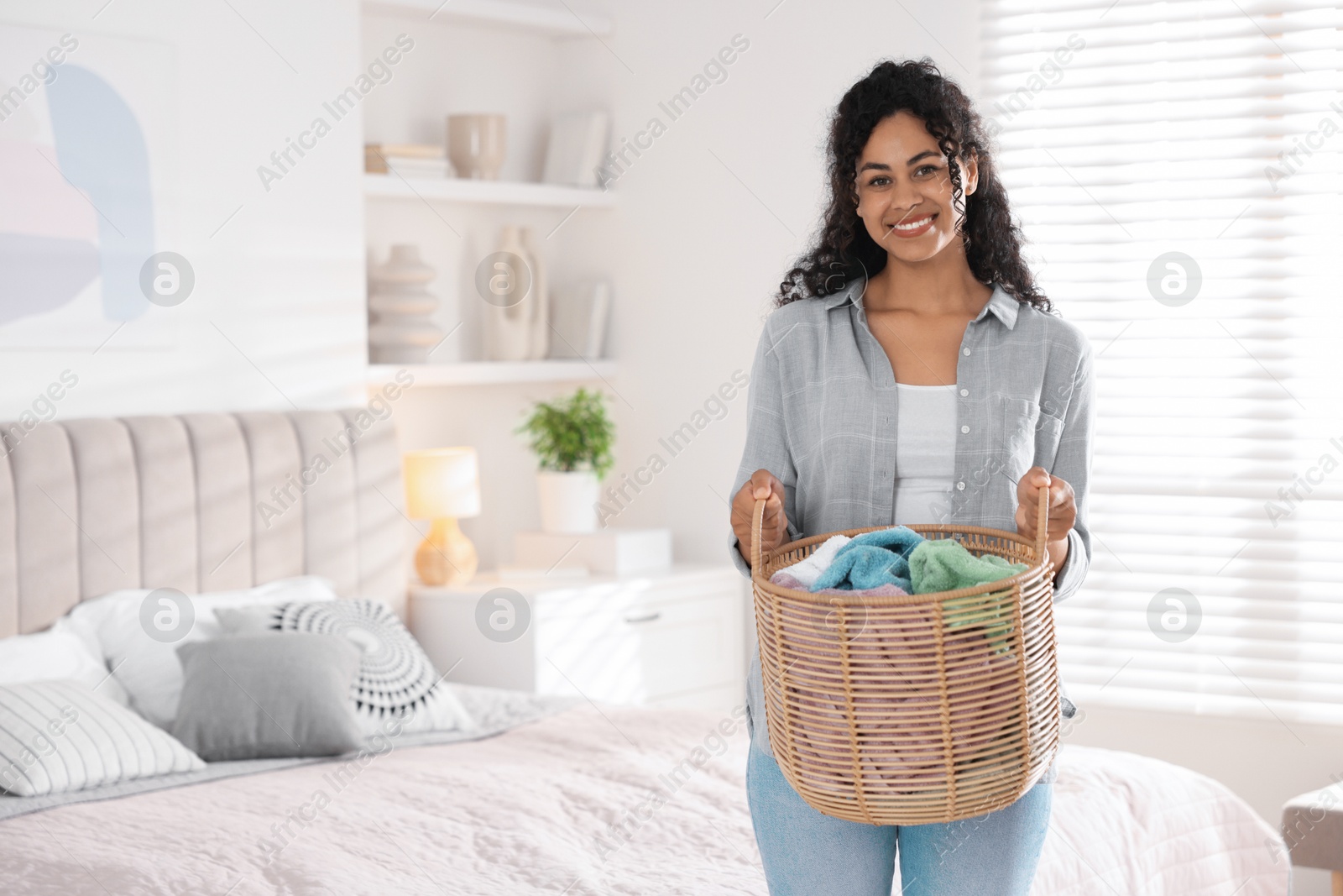 Photo of Happy woman with basket full of laundry in bedroom