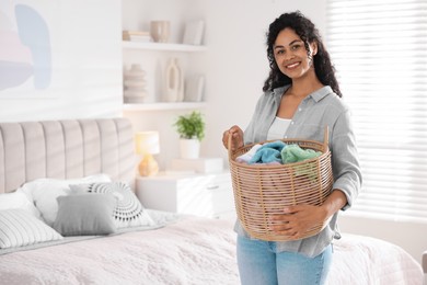 Happy woman with basket full of laundry in bedroom