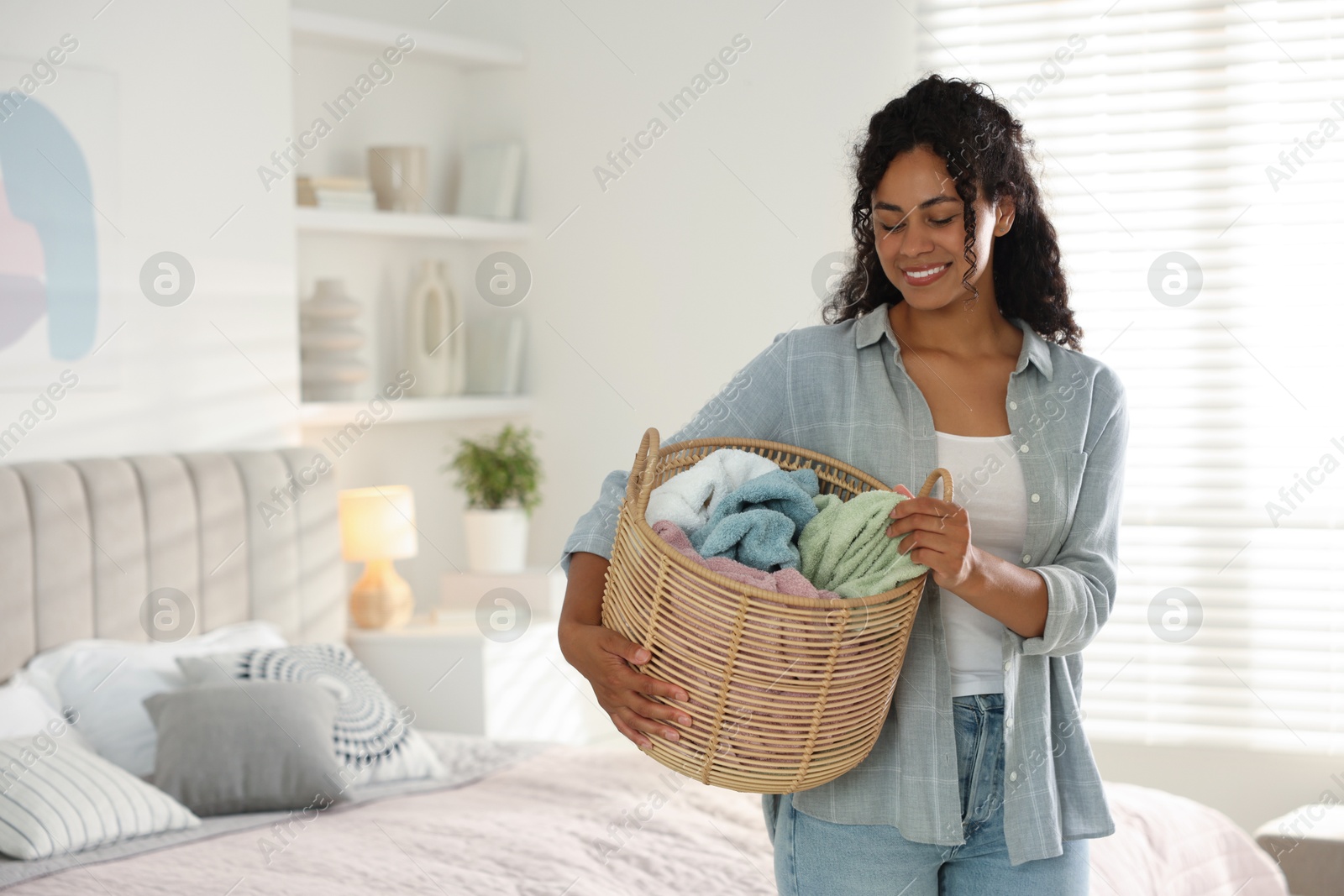 Photo of Happy woman with basket full of laundry in bedroom