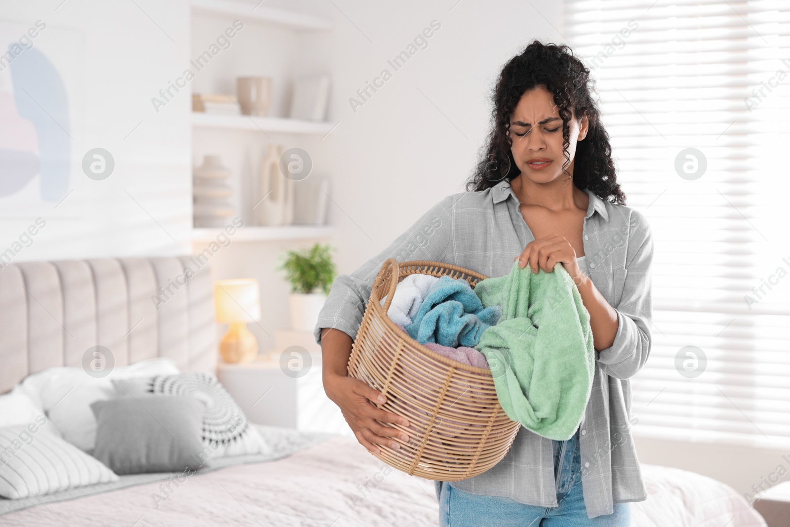 Photo of Displeased woman with basket full of laundry in bedroom