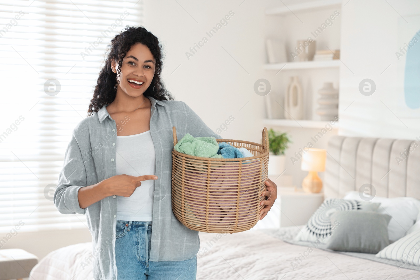 Photo of Happy woman with basket full of laundry in bedroom