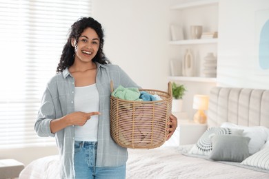 Photo of Happy woman with basket full of laundry in bedroom