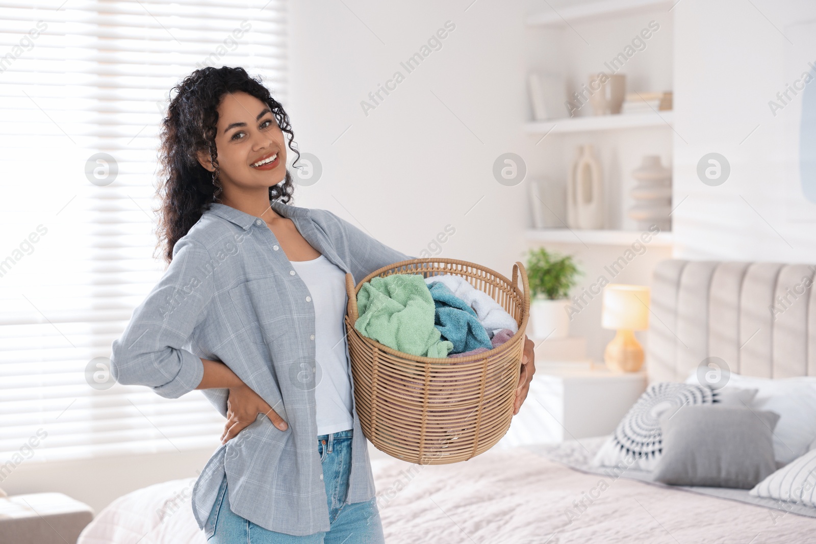 Photo of Happy woman with basket full of laundry in bedroom