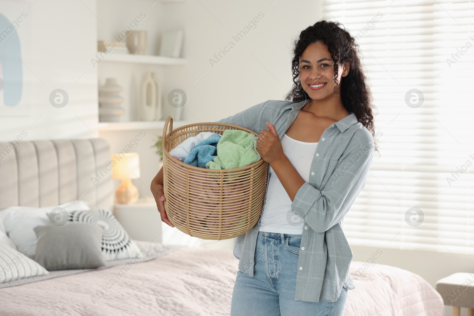 Photo of Happy woman with basket full of laundry in bedroom