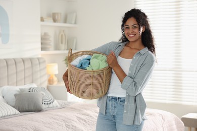 Happy woman with basket full of laundry in bedroom