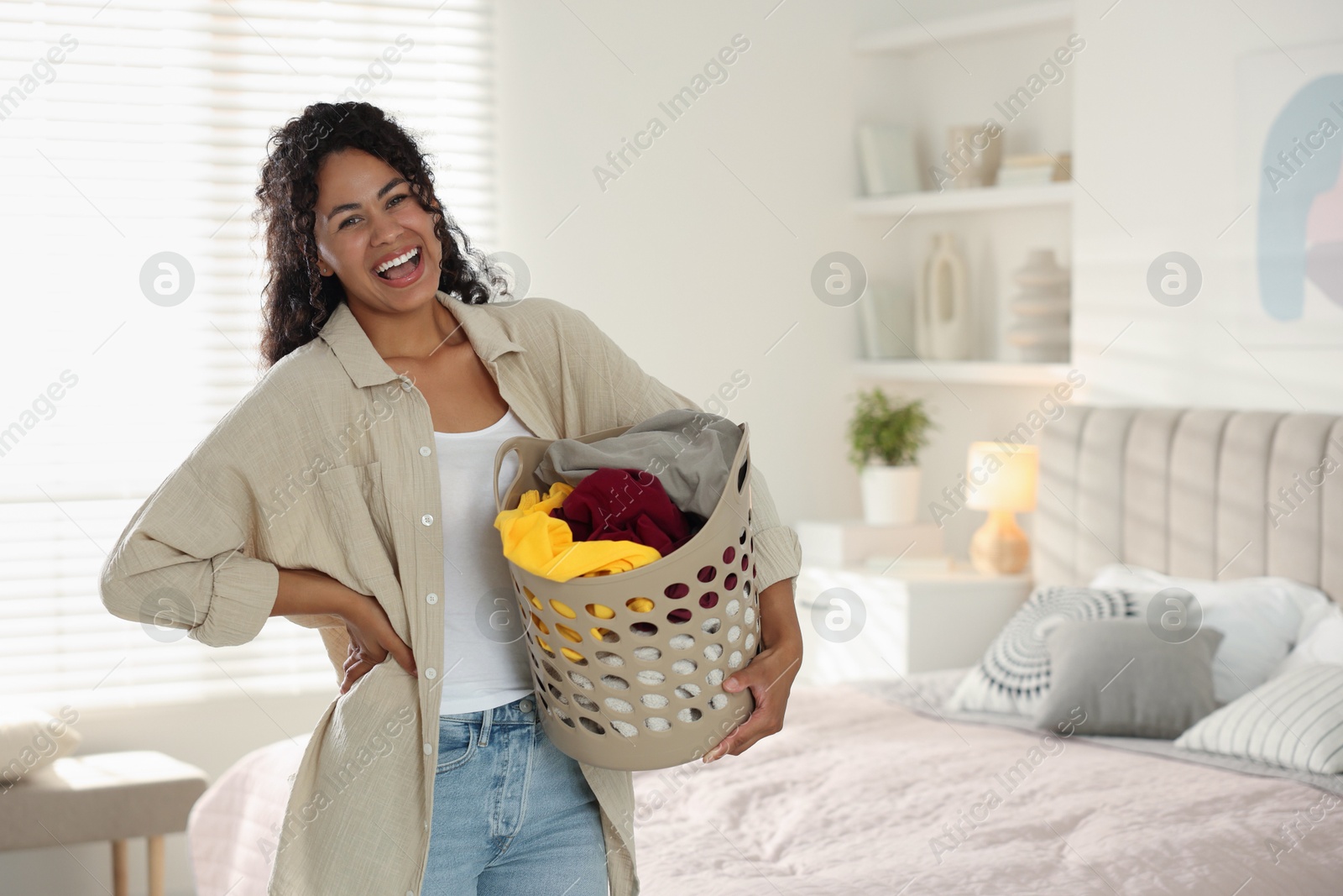 Photo of Happy woman with basket full of laundry in bedroom