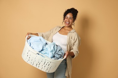 Happy woman with basket full of laundry on beige background