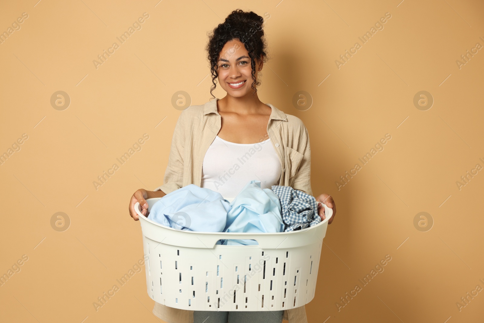 Photo of Happy woman with basket full of laundry on beige background