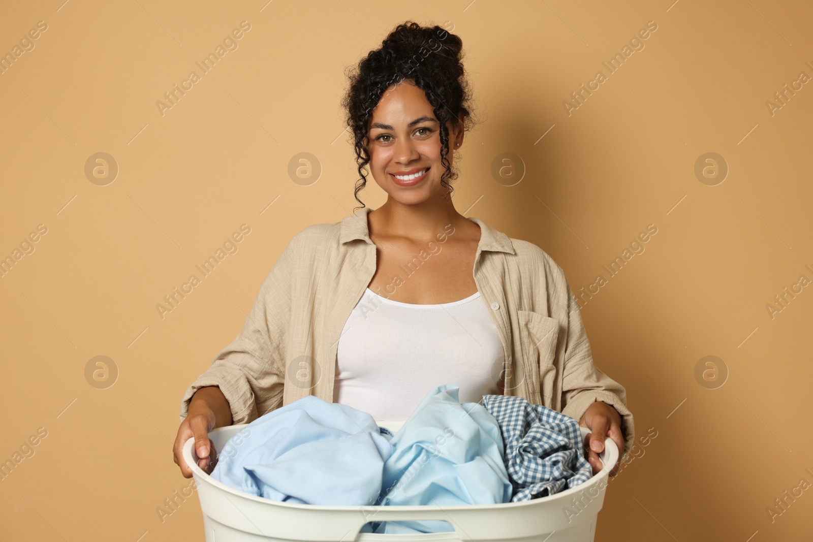 Photo of Happy woman with basket full of laundry on beige background