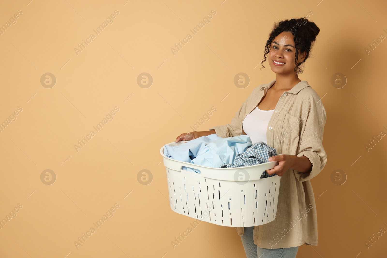 Photo of Happy woman with basket full of laundry on beige background, space for text