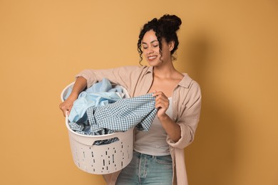 Happy woman with basket full of laundry on beige background