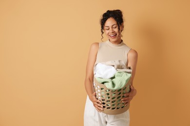 Happy woman with basket full of laundry on beige background, space for text