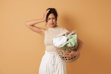 Tired woman with basket full of laundry on beige background