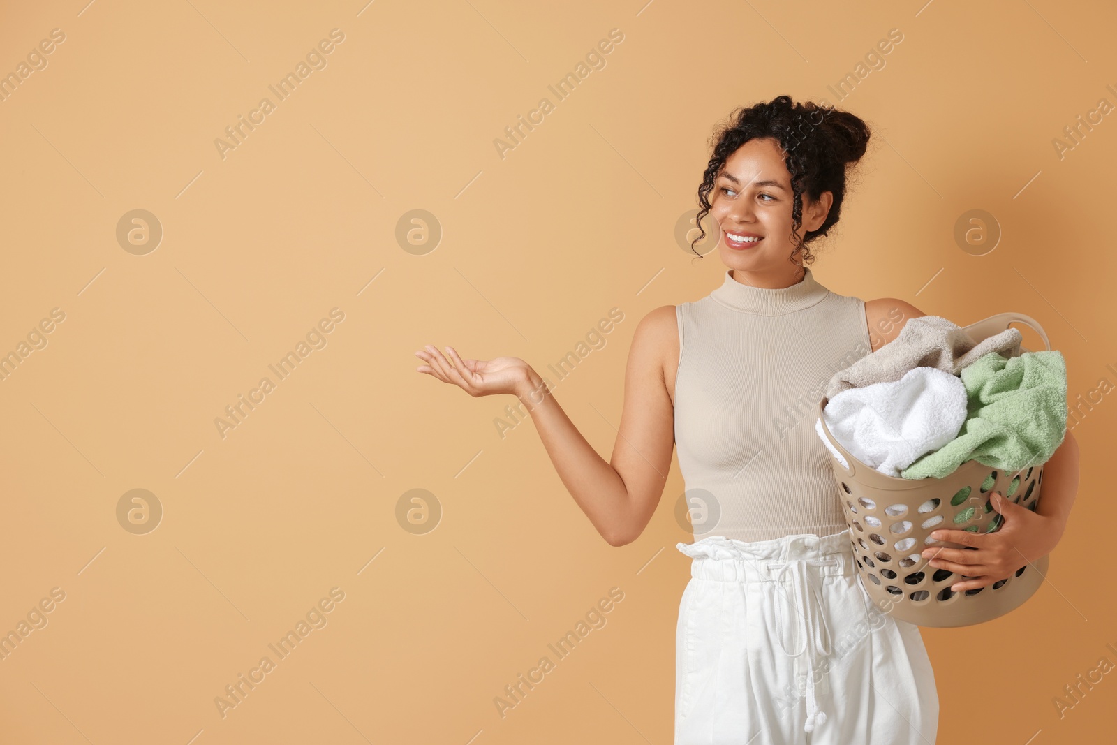 Photo of Happy woman with basket full of laundry on beige background, space for text