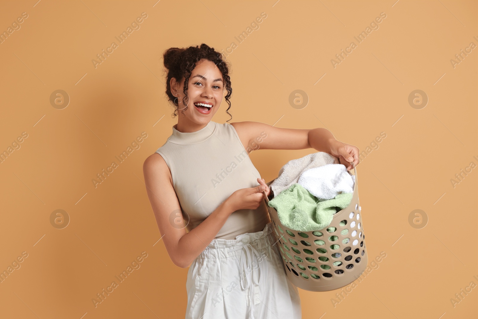 Photo of Happy woman with basket full of laundry on beige background