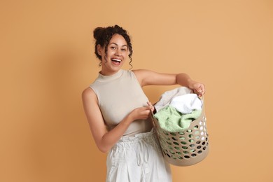 Happy woman with basket full of laundry on beige background