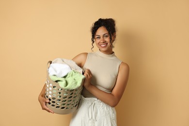 Photo of Happy woman with basket full of laundry on beige background