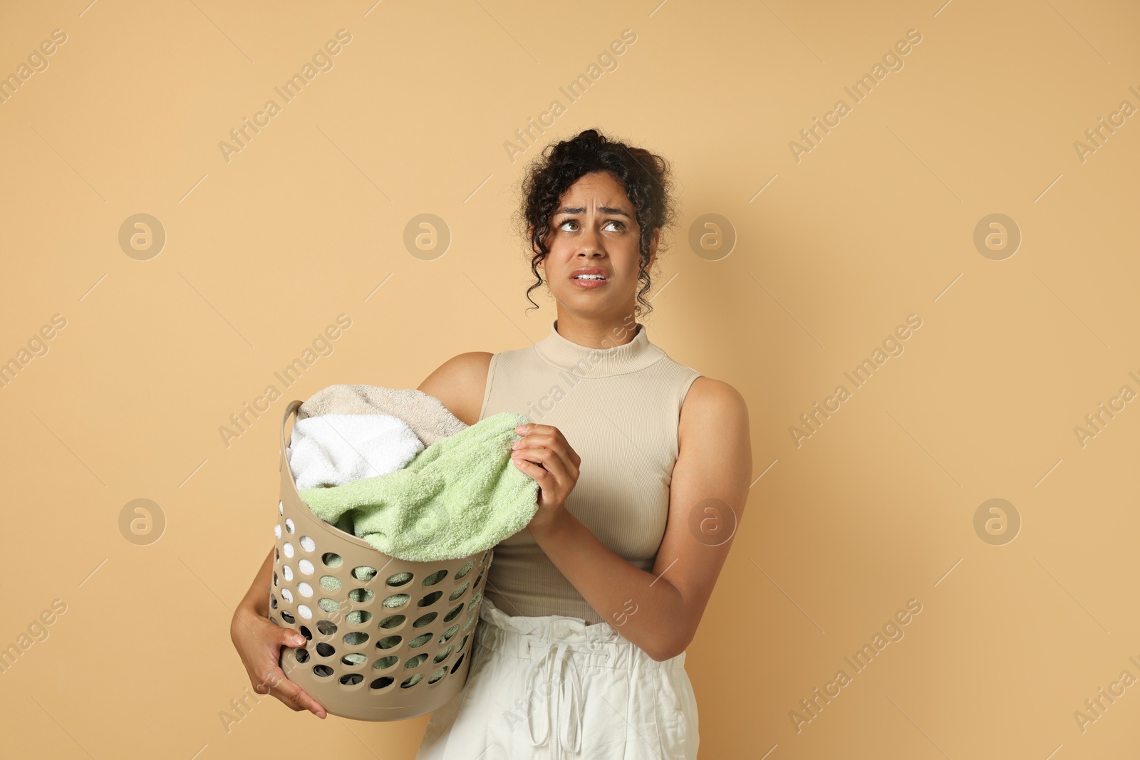 Photo of Displeased woman with basket full of laundry on beige background