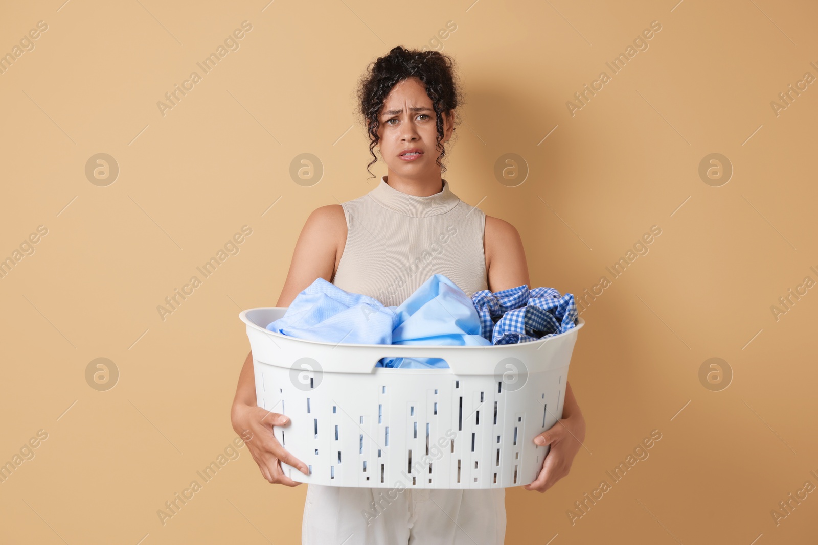 Photo of Displeased woman with basket full of laundry on beige background