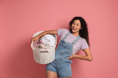 Photo of Happy woman with basket full of laundry on pink background