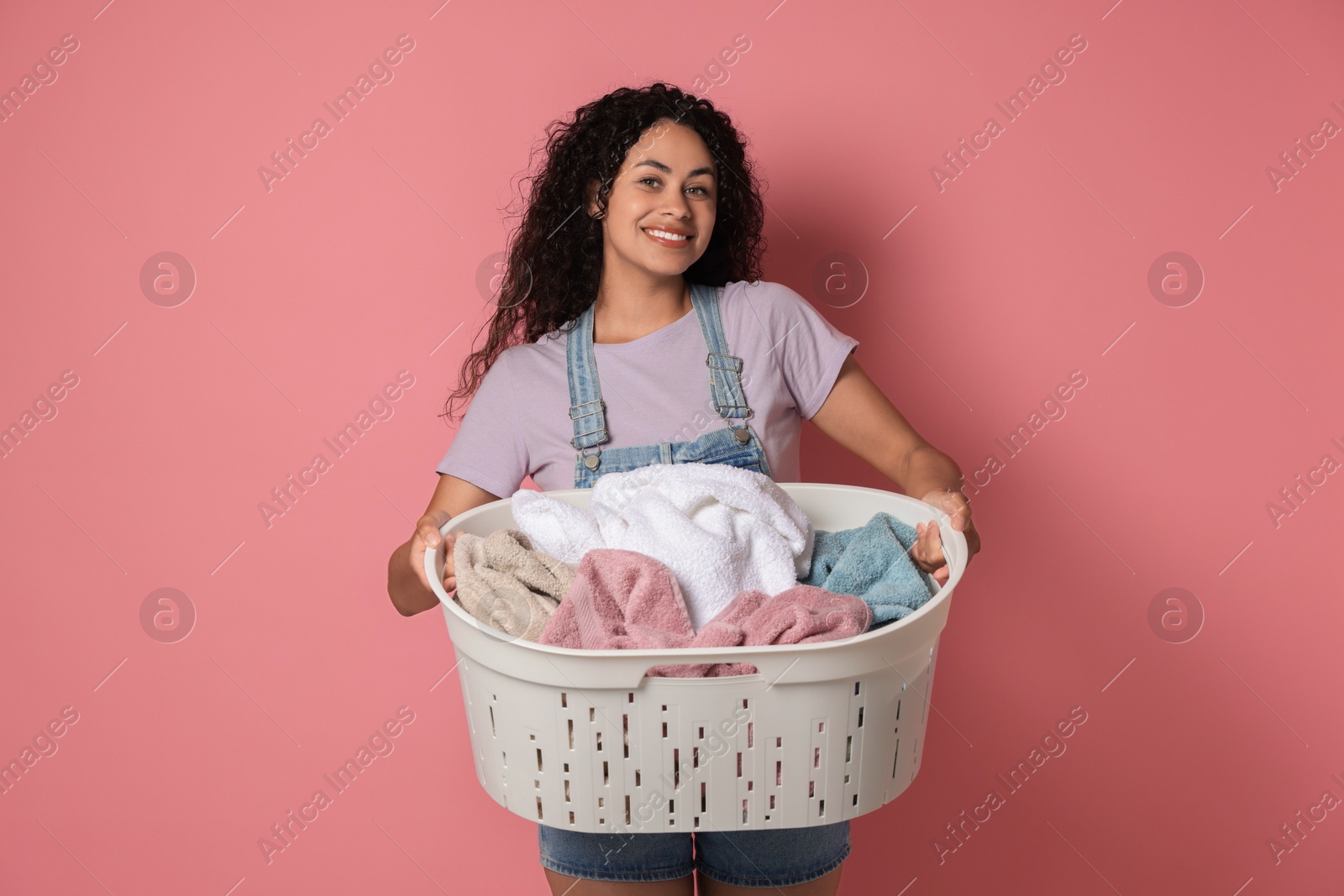 Photo of Happy woman with basket full of laundry on pink background